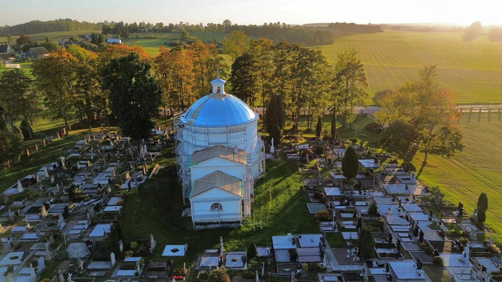 Bažnyčia ir kapinės plačiame rudens kraštovaizdyje.